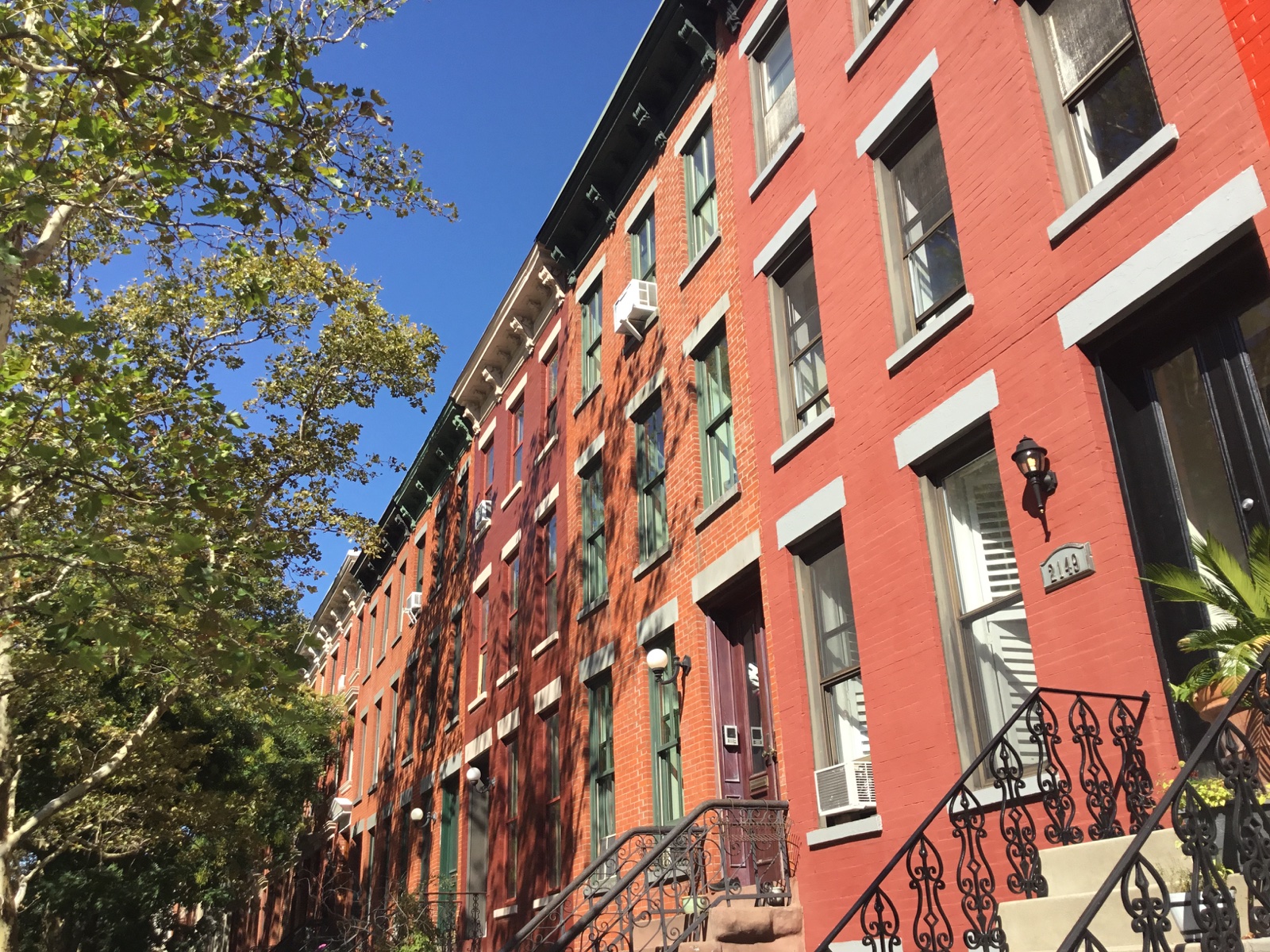 Sunlit brick row houses with stone lintels, raised stoops and iron railings on 45th Avenue